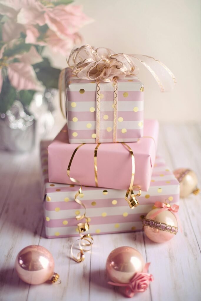 Home Charming Christmas presents wrapped in pink and gold with festive ornaments on a wooden table.